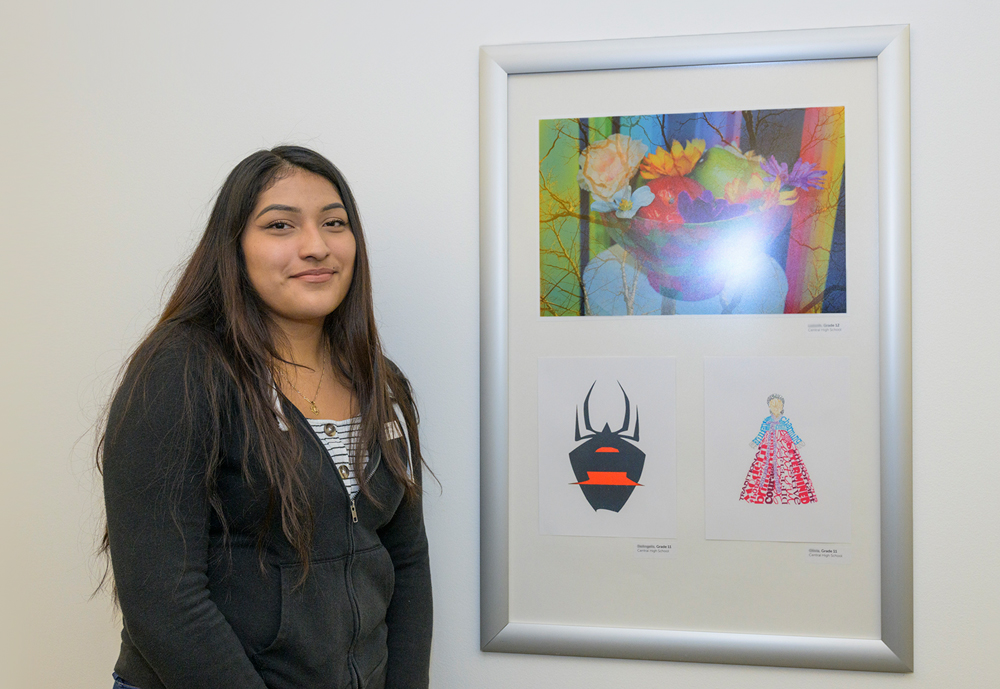 high school student stands next to her artwork in an exhibition