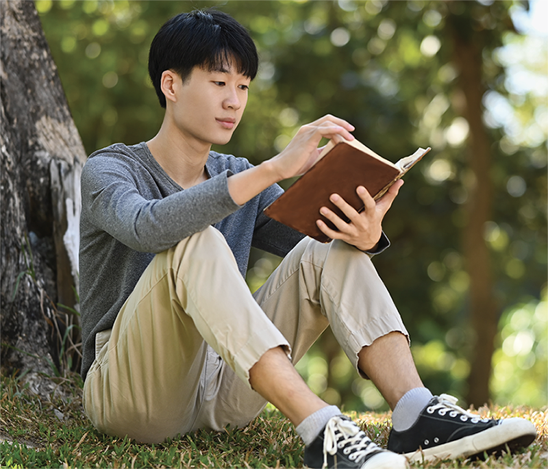 teenager sits by tree reading