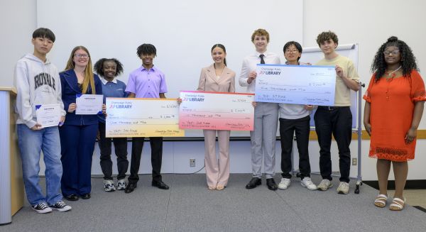 High school students stand together smiling and hold giant checks