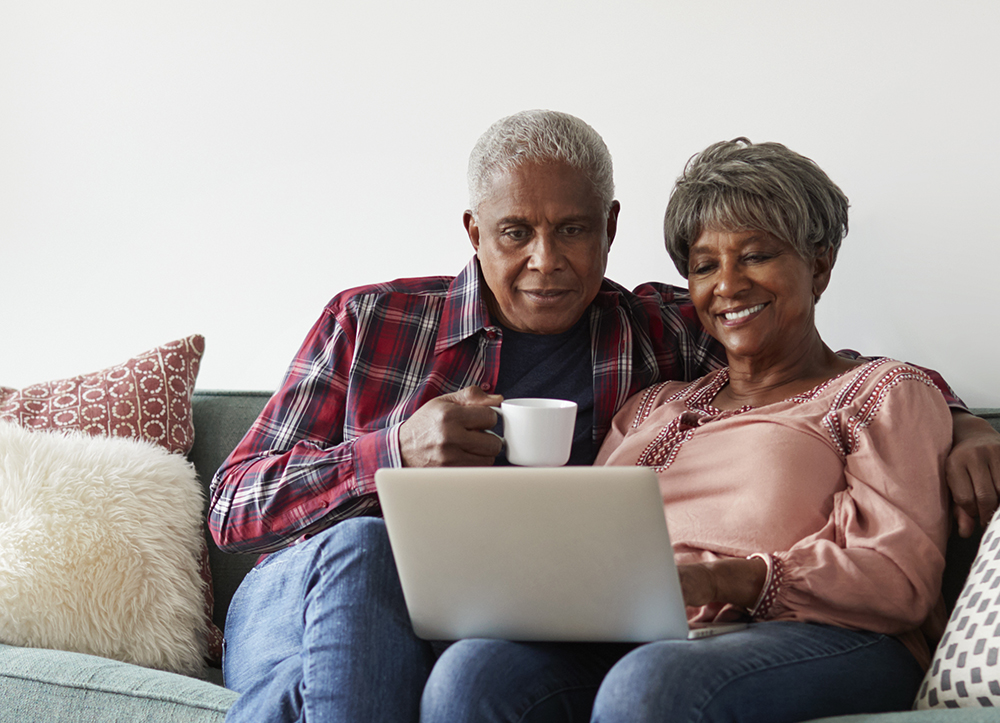 A senior couple relaxing on their couch with coffee looking at a laptop computer